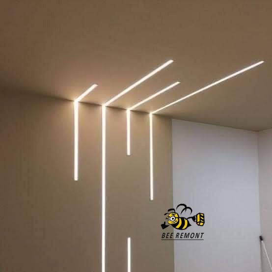 Nowoczesne oświetlenie LED wpuszczone w sufit i ścianę, tworzące pionowe i poziome linie światła w minimalistycznym wnętrzu, z widocznym logo firmy w prawym dolnym rogu.