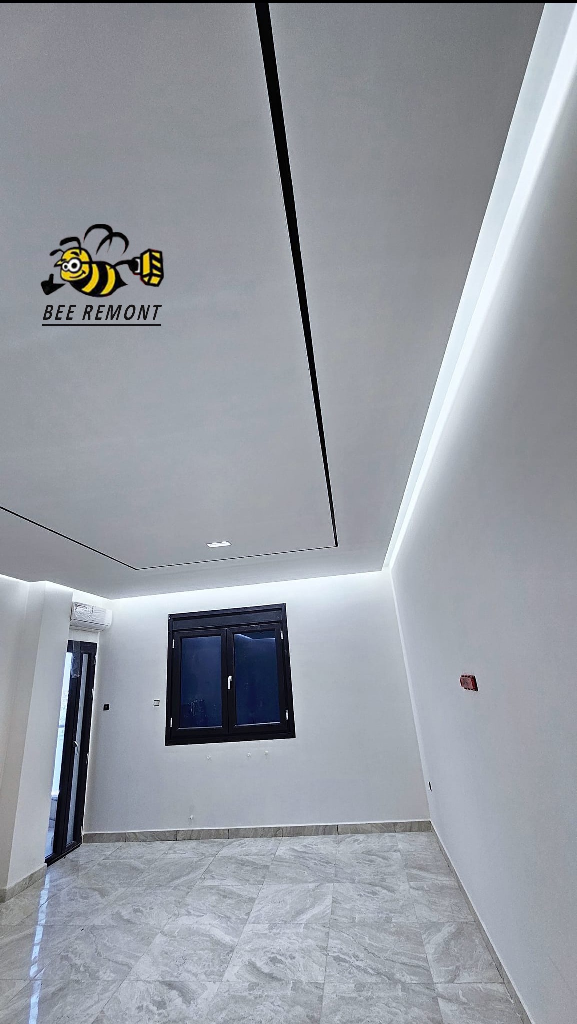 Białe wnętrze z szarymi płytkami podłogowymi, czarnymi ramami okiennymi i sufitem z dekoracyjnymi czarnymi liniami oraz oświetleniem LED. W lewym górnym rogu widoczne logo firmy 'BEE REMONT'...