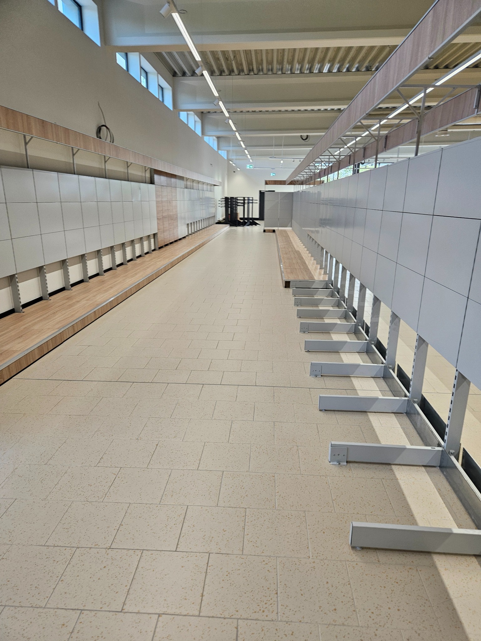 Wnętrze hali magazynowej lub sklepu w trakcie sprzątania po remoncie, widoczne puste regały i czysta podłoga z płytek.