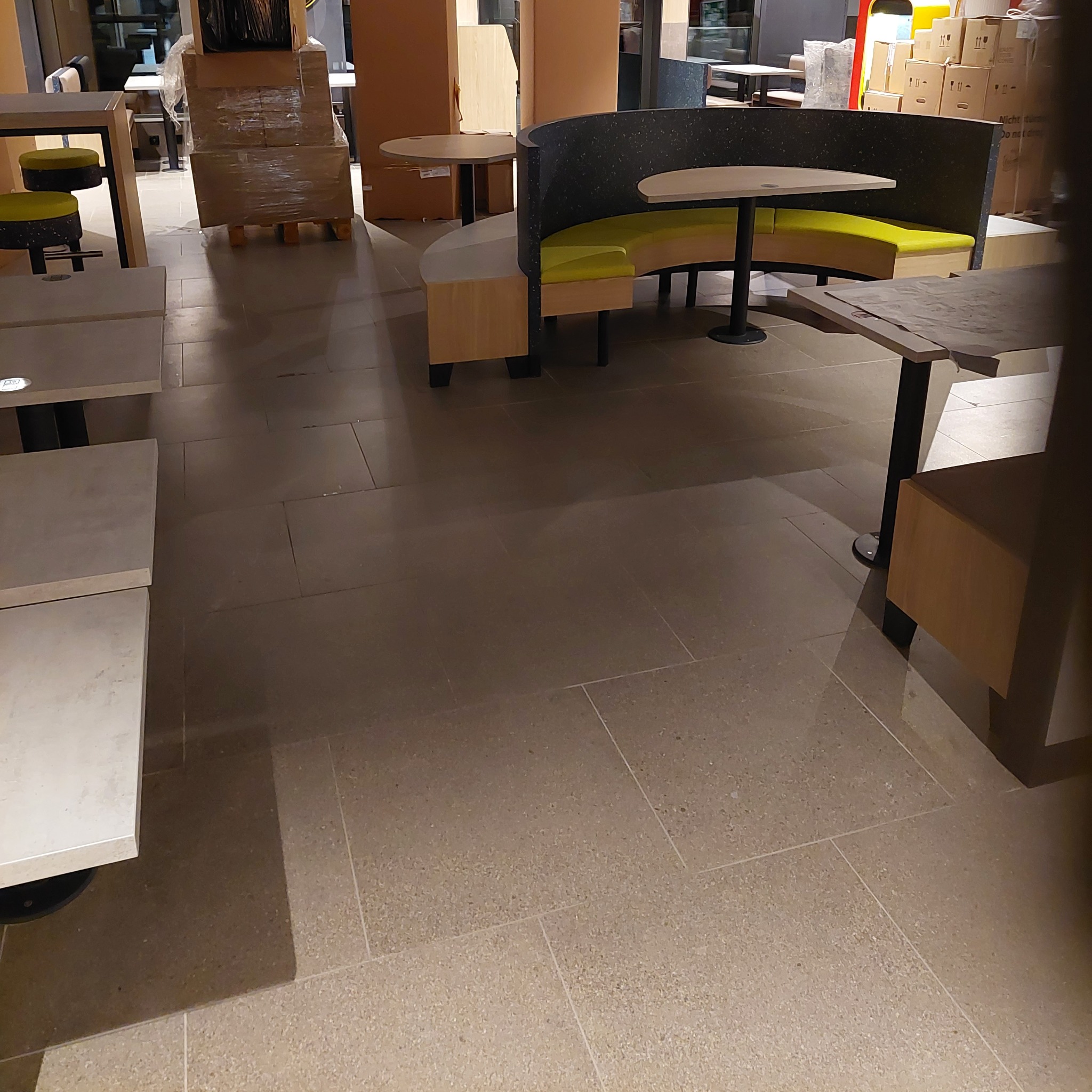 Nowe meble restauracyjne, w tym półokrągłe loże z żółtymi siedziskami i stoły z marmurowymi blatami, rozstawione na podłodze z płytek w trakcie aranżacji przestrzeni.