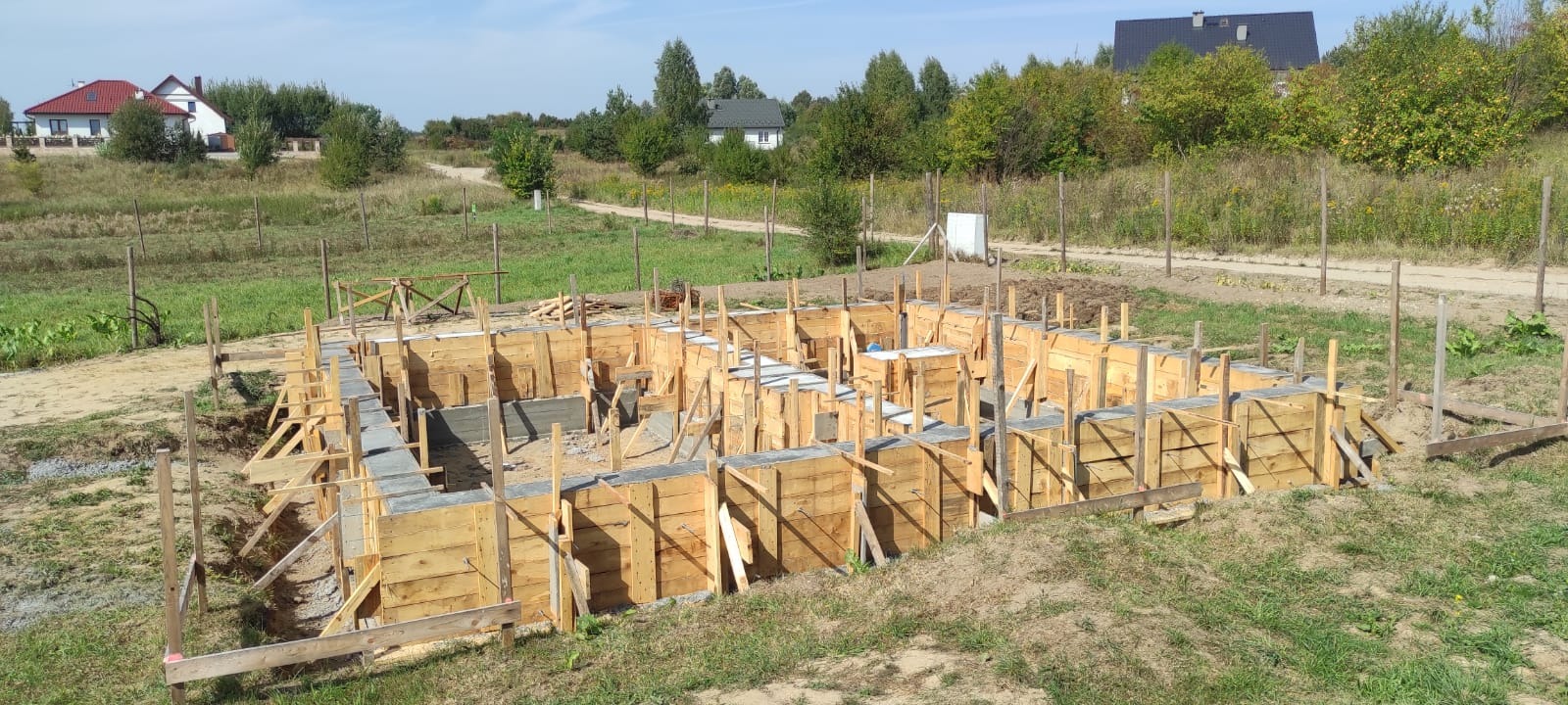 Wylane fundamenty domu jednorodzinnego, drewniane szalunki, widok z góry, teren budowy z widokiem na okoliczne domy i drzewa.