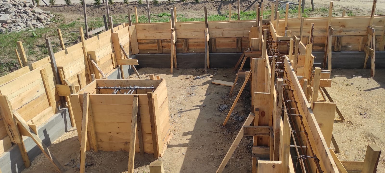 Szczegółowe ujęcie szalunku fundamentów z widocznym zbrojeniem, przygotowanego do zalania betonem, z drewnianymi podporami stabilizującymi konstrukcję.