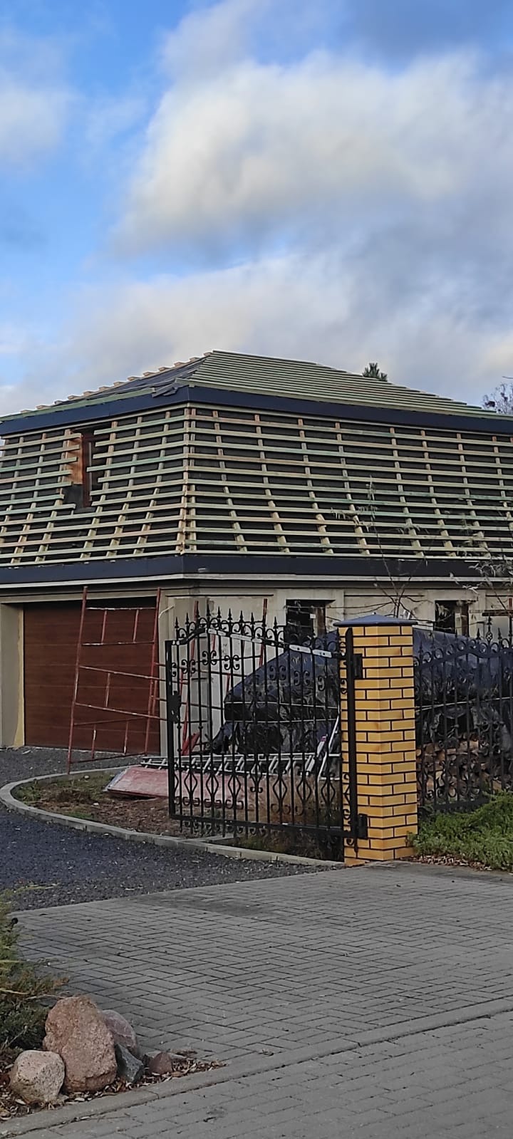 Konstrukcja więźby dachowej z łatami na domu jednorodzinnym, widok z poziomu chodnika, brama w tle.