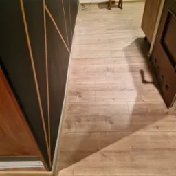 Ukończona podłoga z paneli drewnopodobnych, widoczna ściana z geometrycznym wzorem w kolorze czarnym i złotym oraz fragment otwartych drzwi.