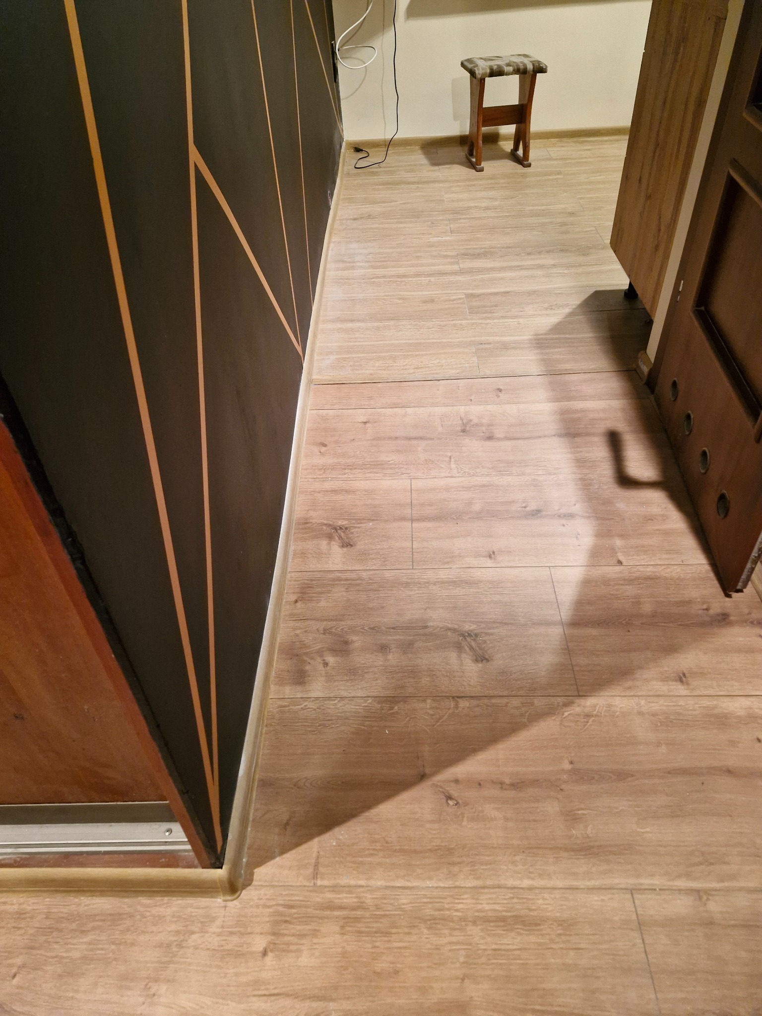 Ukończona podłoga z paneli drewnopodobnych, widoczna ściana z geometrycznym wzorem w kolorze czarnym i złotym oraz fragment otwartych drzwi.