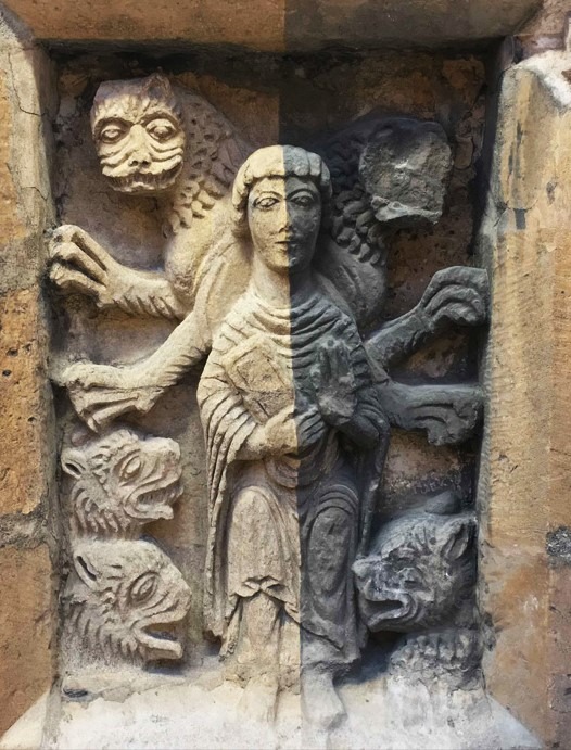 Kamienna płaskorzeźba przedstawiająca postać centralną z księgą, otoczoną przez trzy rzeźby głow zwierzęcych i postać z pazurami, całość umieszczona w kamiennej wnęce z wyraźnymi śladami erozji...