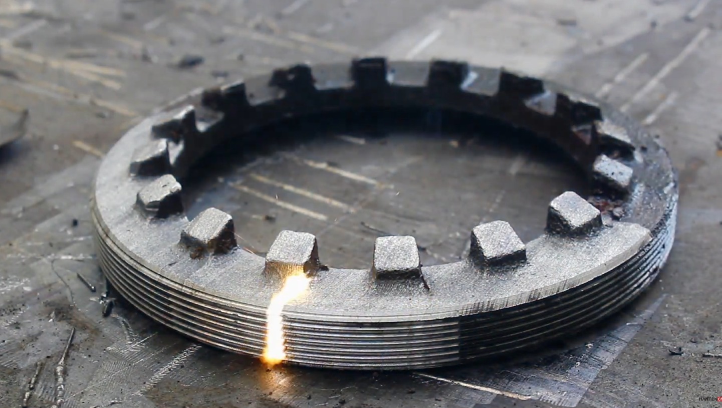 Metalowy pierścień z ząbkami poddawany obróbce termicznej, widoczny płomień i iskry.