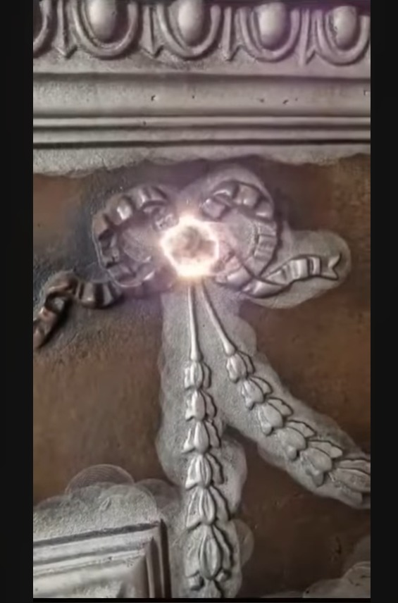 Detal dekoracyjny w postaci wstążki i girlandy na zabytkowej powierzchni, oświetlony punktowo, z widocznymi śladami upływu czasu.