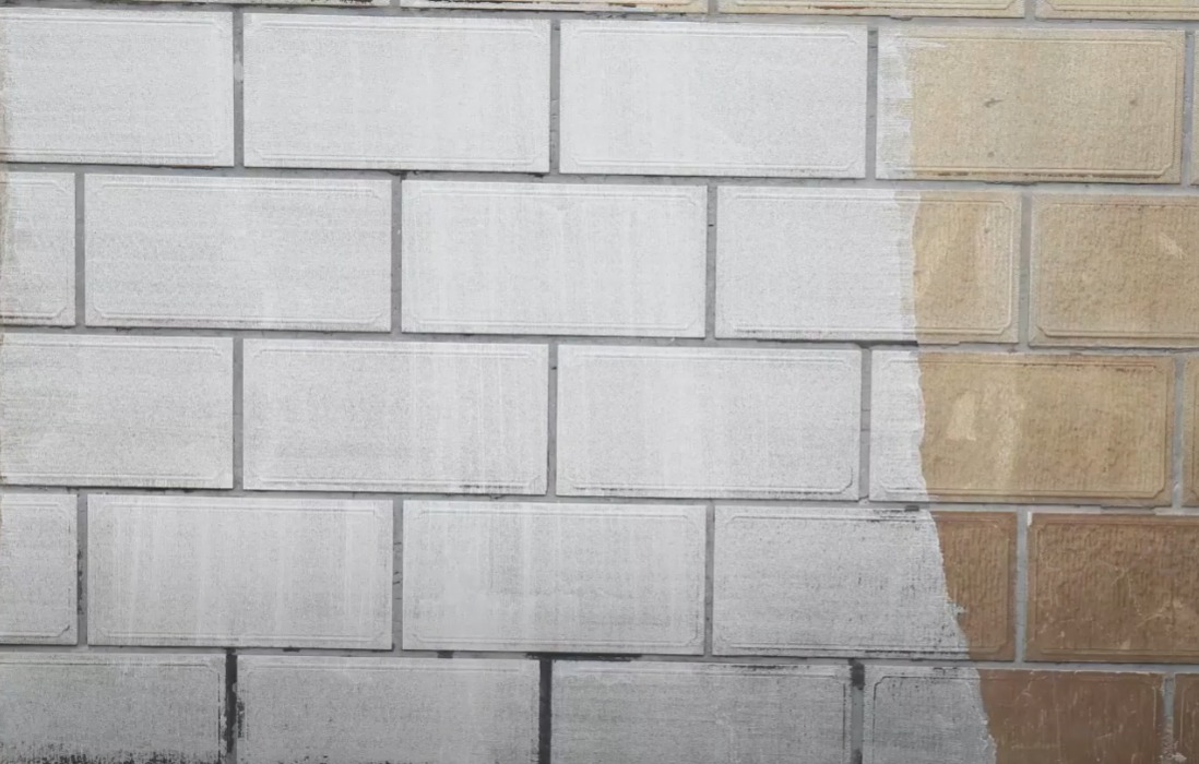 Fragment odrestaurowanej ceglanej ściany, połowa wyczyszczona, ukazująca oryginalny kolor i fakturę cegieł, druga połowa pokryta szarym nalotem.