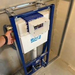 Dawid Woś - Stelaż podtynkowy WC marki Roca zamontowany w łazience w Środzie Śląskiej. Widoczna instalacja wodno-kanalizacyjna i metalowa konstrukcja mocująca.