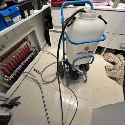 Renova - Urządzenie PIKO-INSTAL do płukania instalacji grzewczej, podłączone do rozdzielacza ogrzewania podłogowego z czerwonymi i niebieskimi rurami, w domowej garderobie.