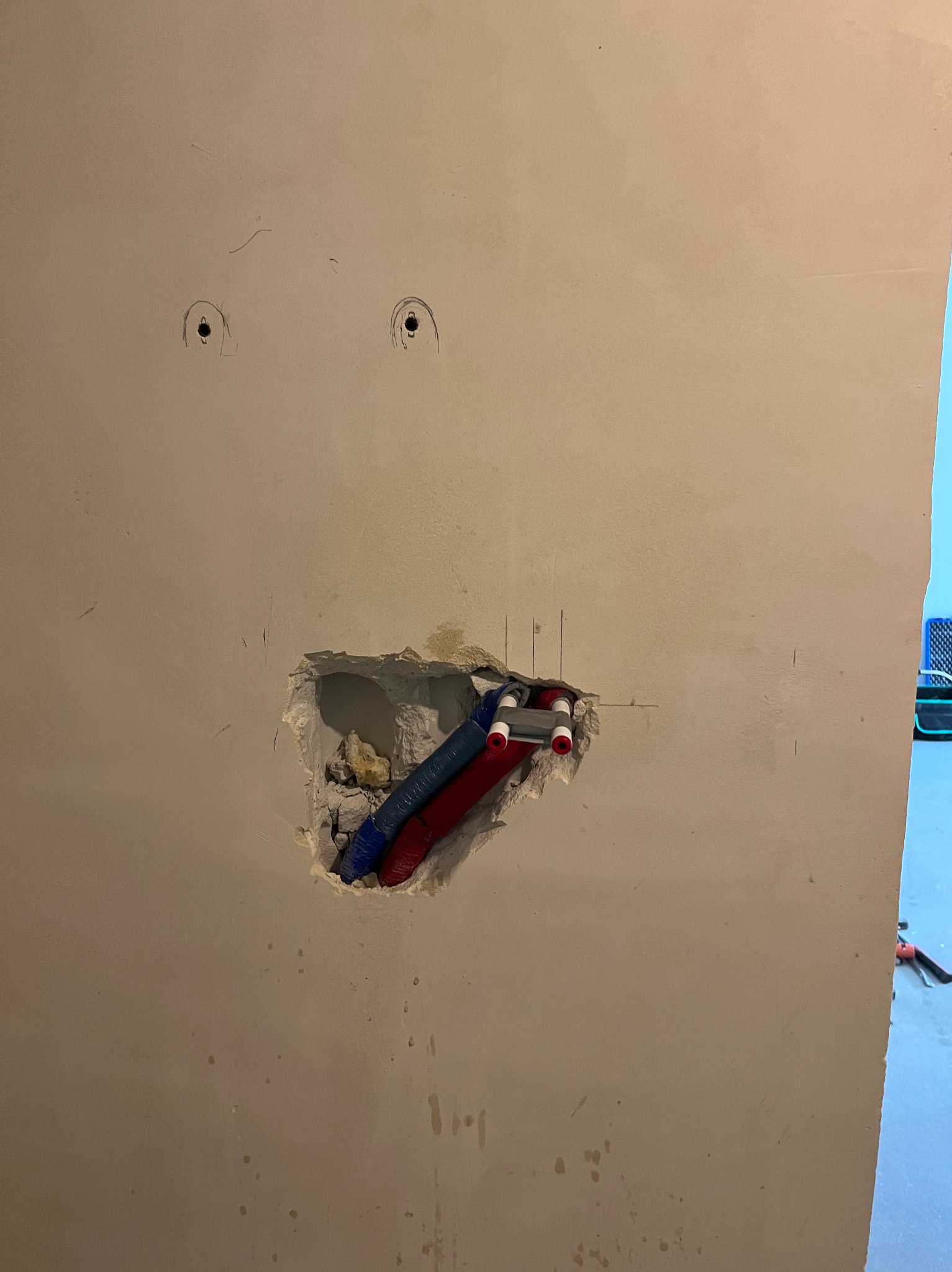 Ściana z otworem, w którym widoczne są rury instalacji wodnej (czerwone i niebieskie) z białymi końcówkami. Nad otworem zaznaczone miejsca na punkty instalacji.