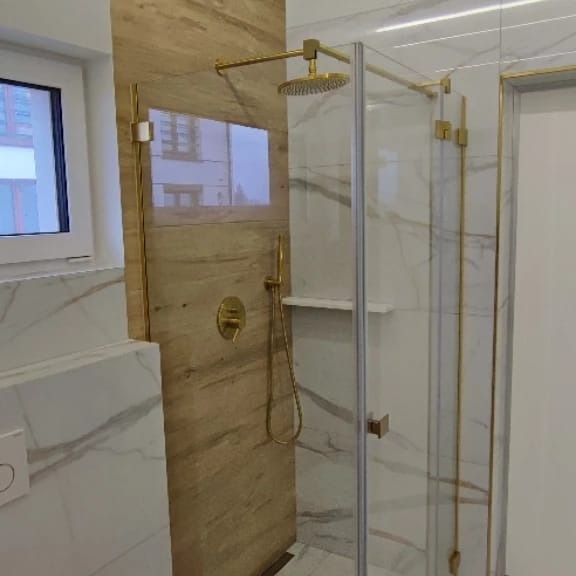 Nowoczesna łazienka z kabiną prysznicową typu walk-in, wykończona płytkami imitującymi marmur i drewno, z armaturą w kolorze złotym.