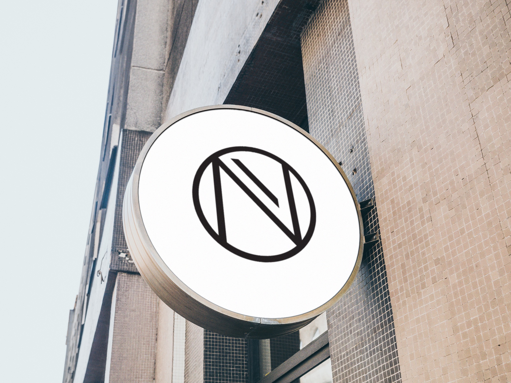 Okrągły szyld z abstrakcyjnym logo na elewacji budynku z mozaikową fakturą.