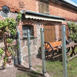 Stal Zachodniopomorskie - Montaż słupków ogrodzeniowych z metalu na tle ceglanego budynku z elementami kamiennymi i dekoracyjnym wozem.