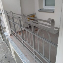 Stal Zachodniopomorskie - Szara metalowa balustrada balkonowa z dekoracyjnymi elementami w kształcie półkola, widoczna z bliska, z oknem w tle.