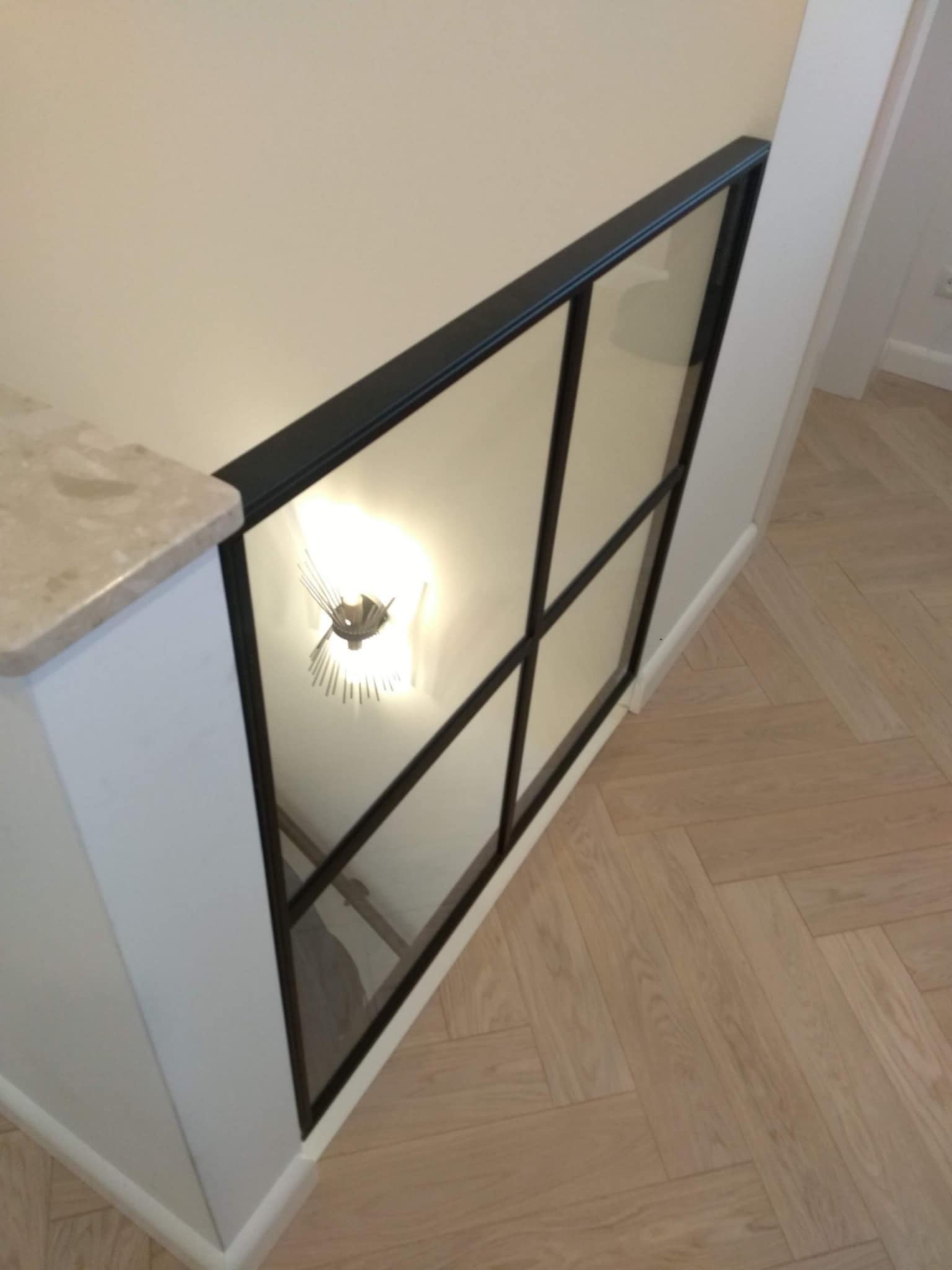 Szklana balustrada schodowa z czarnymi szprosami, widok z góry na parkiet ułożony w jodełkę.