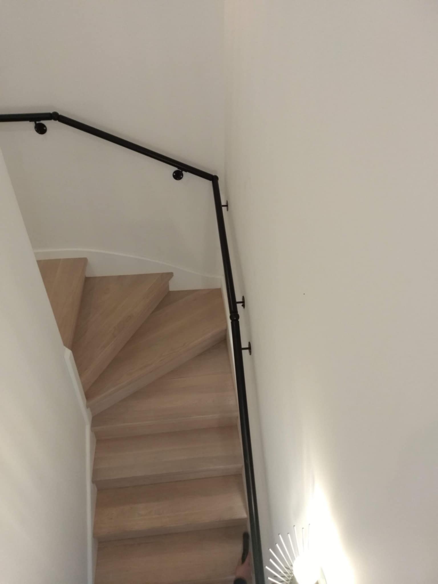 Wewnętrzne schody drewniane z czarną, metalową poręczą zamocowaną do ściany, widok z góry.