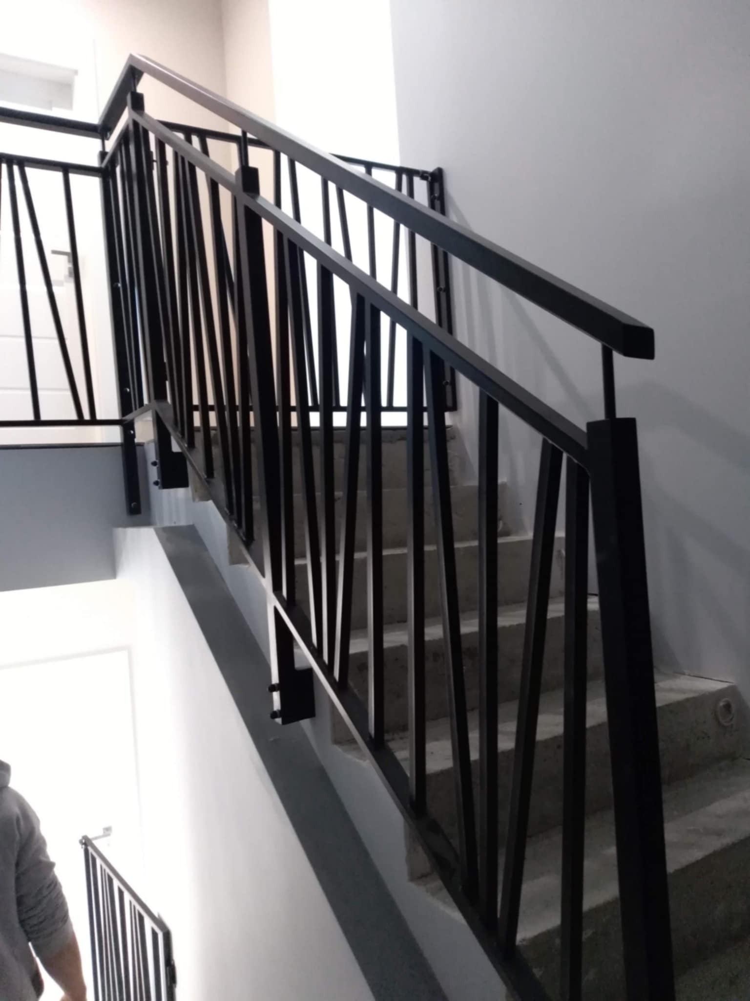 Nowoczesne czarne poręcze schodowe z pionowymi prętami na betonowych schodach wewnątrz budynku, widok z dołu.
