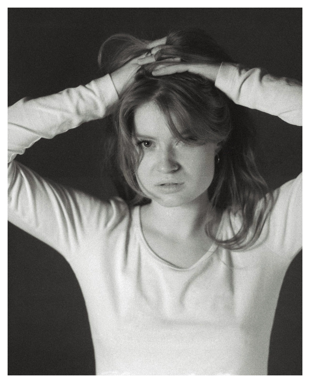 Portret młodej kobiety z rękami we włosach, wyraz zamyślenia na twarzy, czarno-białe zdjęcie w stylu vintage.