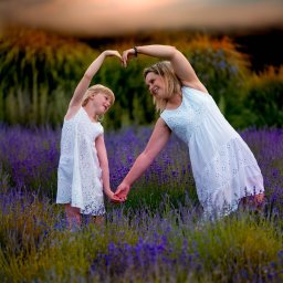 Miroslaw Kocurek Photography - Matka i córka w białych sukienkach stoją na polu lawendy, trzymają się za ręce i tworzą kształt serca z ramion nad głowami, zachód słońca w tle.
