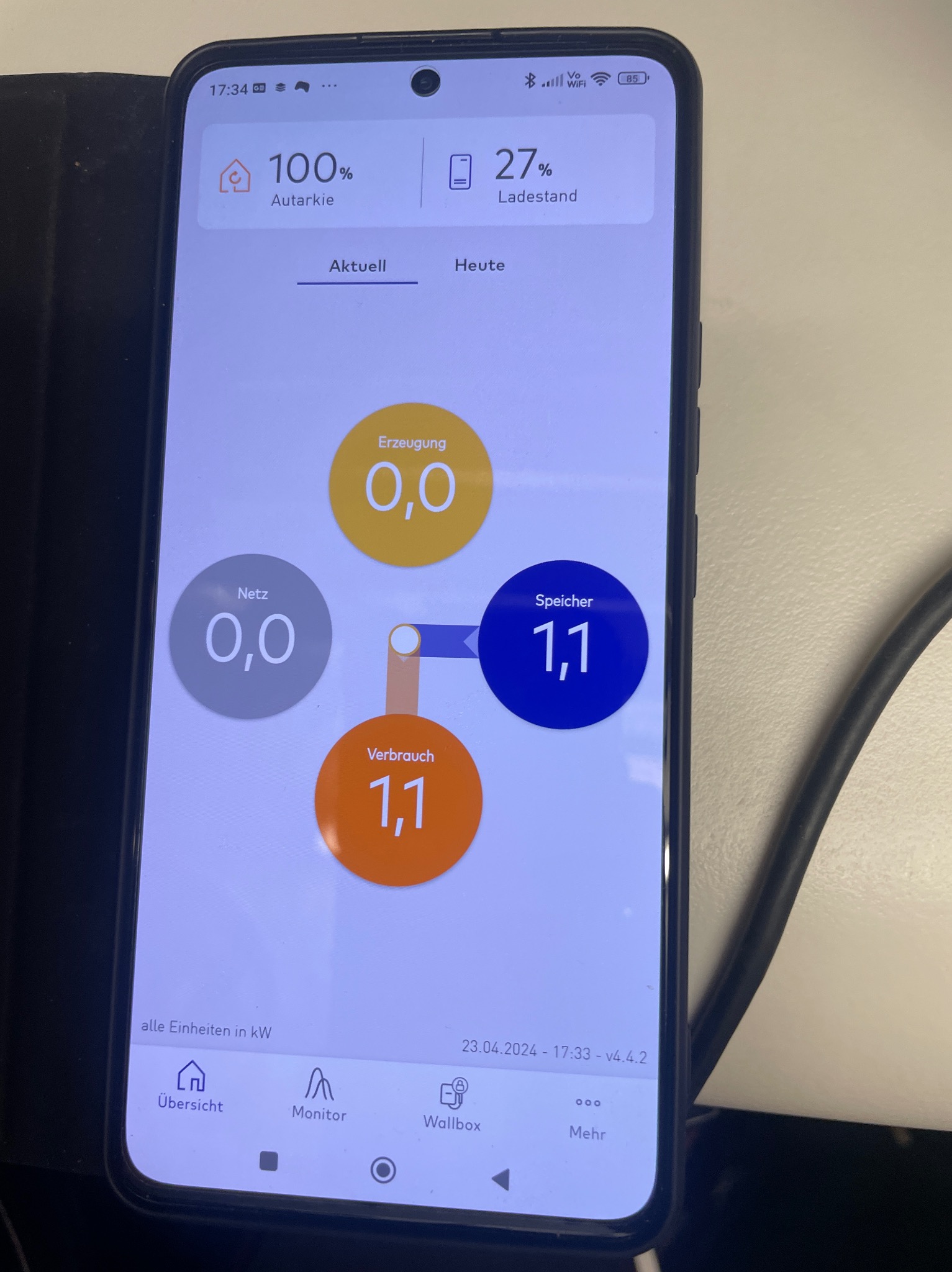 Ekran smartfona prezentujący aplikację do monitorowania zużycia energii z fotowoltaiki, z danymi o produkcji, zużyciu i stanie magazynu energii w kW.