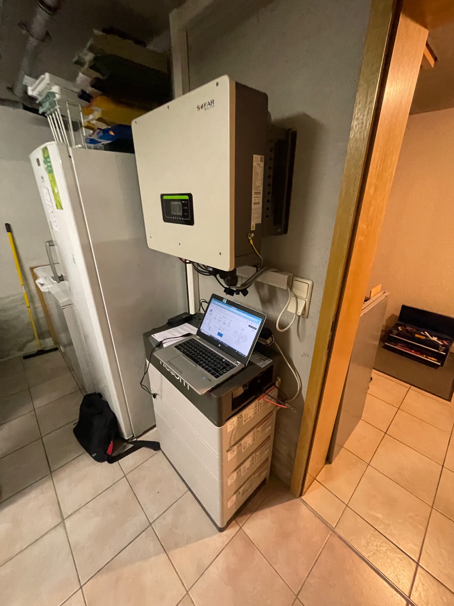 Podłączenie i konfiguracja systemu magazynowania energii w piwnicy, widoczny inwerter Sofar, moduł bateryjny, laptop z oprogramowaniem diagnostycznym i skrzynka narzędziowa w tle.