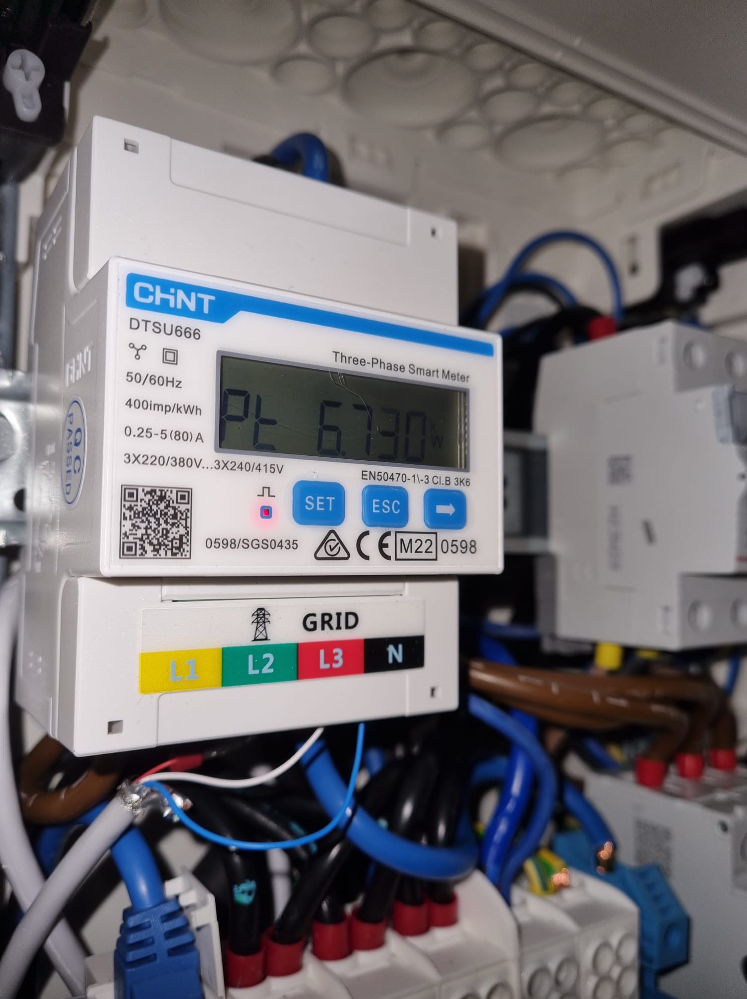 Trójfazowy inteligentny licznik energii CHNT DTSU666 z wyświetlaczem wskazującym zużycie energii, podłączony do instalacji elektrycznej z widocznymi przewodami oznaczonymi kolorami L1, L2, L3 i N.