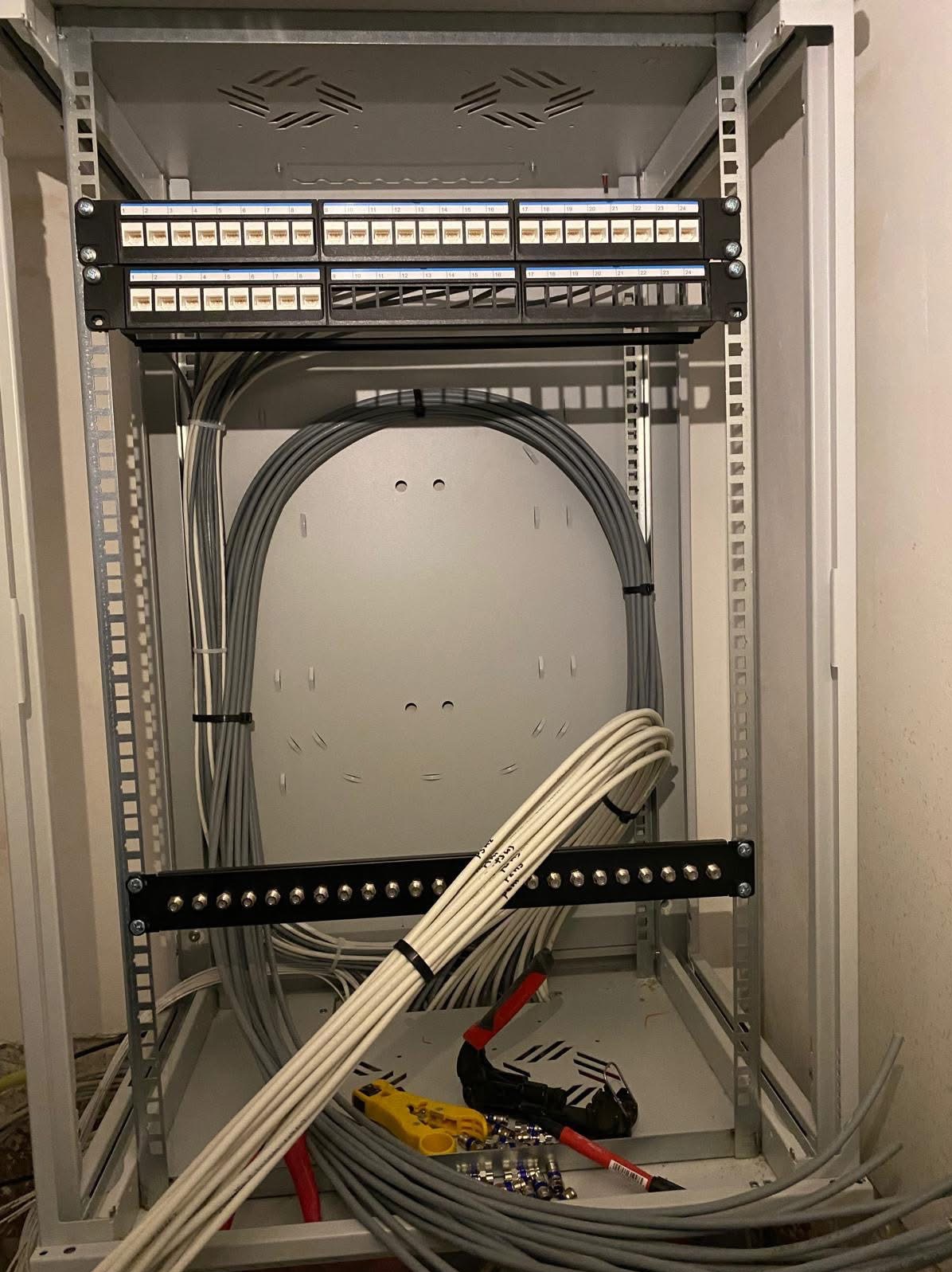 Szafa rack z patch panelem, uporządkowane kable szare i białe, narzędzia do zarabiania kabli na dnie szafy.