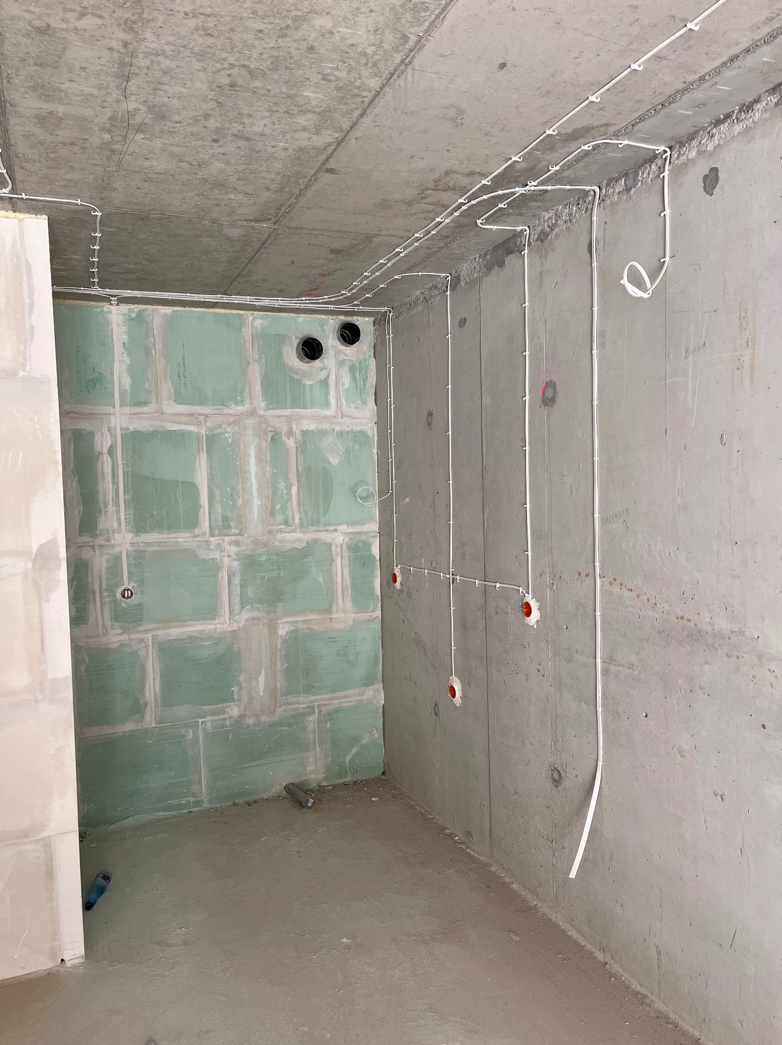 Wnętrze w stanie surowym z widoczną instalacją elektryczną: przewody poprowadzone po ścianach i suficie, puszki instalacyjne, ściany częściowo pokryte płytami gipsowo-kartonowymi.