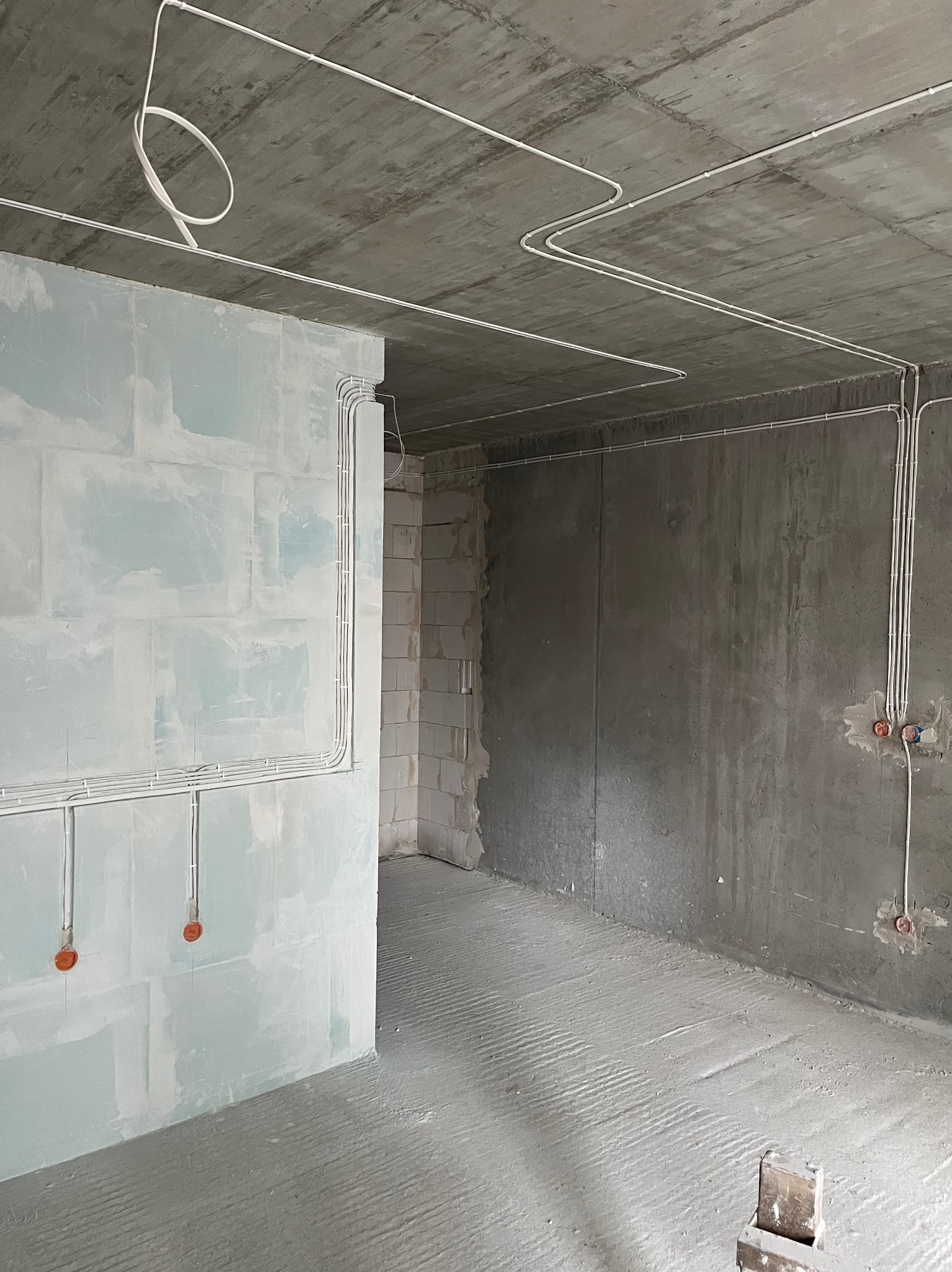 Wnętrze w stanie surowym z rozprowadzonymi przewodami elektrycznymi na ścianach i suficie. Widoczne puszki instalacyjne. Ściany w surowym tynku.