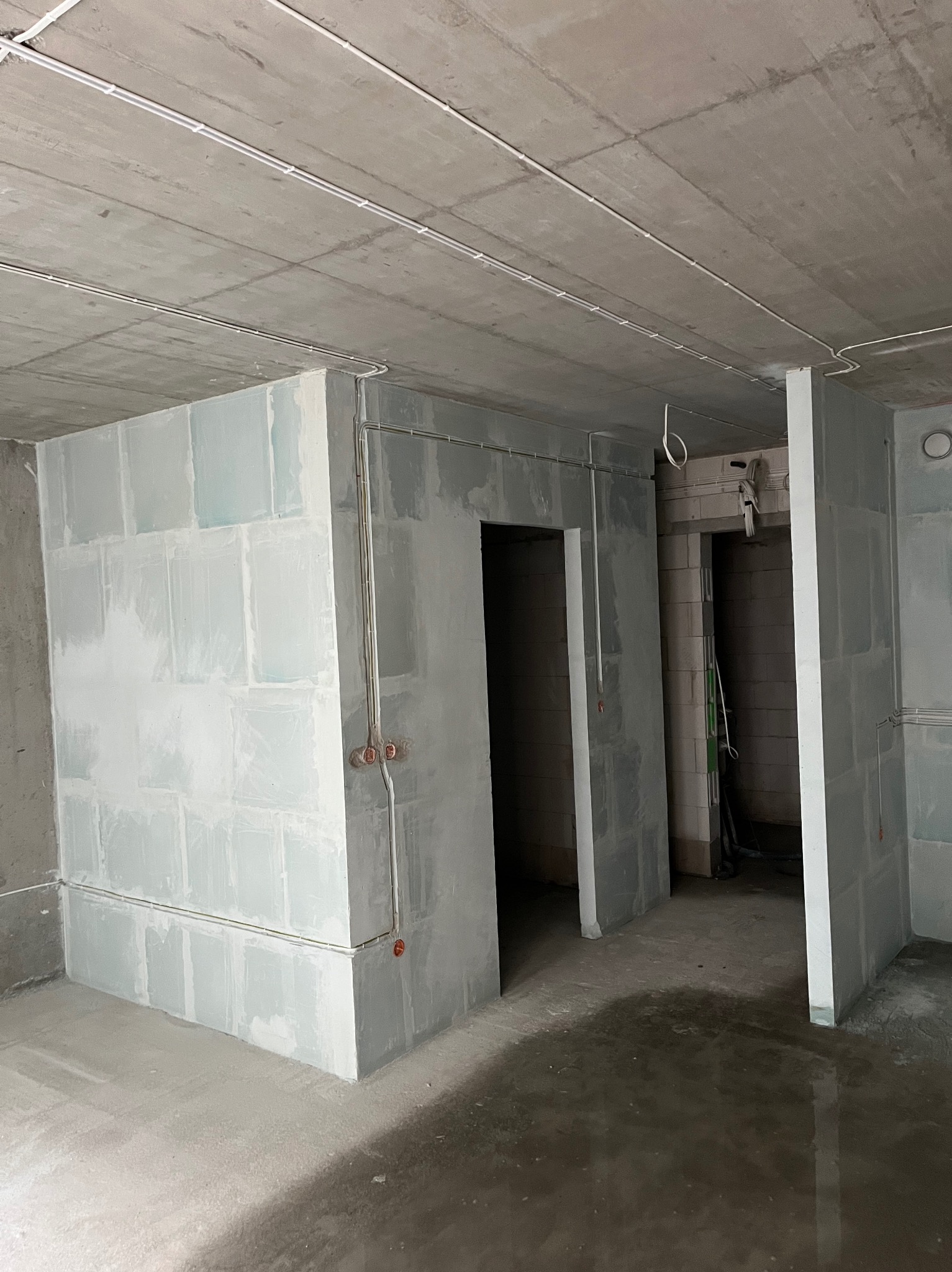 Surowy stan wnętrza: ściany działowe z płyt gipsowych, widoczne kable elektryczne pod sufitem i przy ścianach, brak wykończenia, surowy betonowy strop.