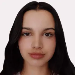 Portret młodej kobiety o ciemnych włosach, brązowych oczach i delikatnym makijażu, z widocznym znamieniem na policzku.