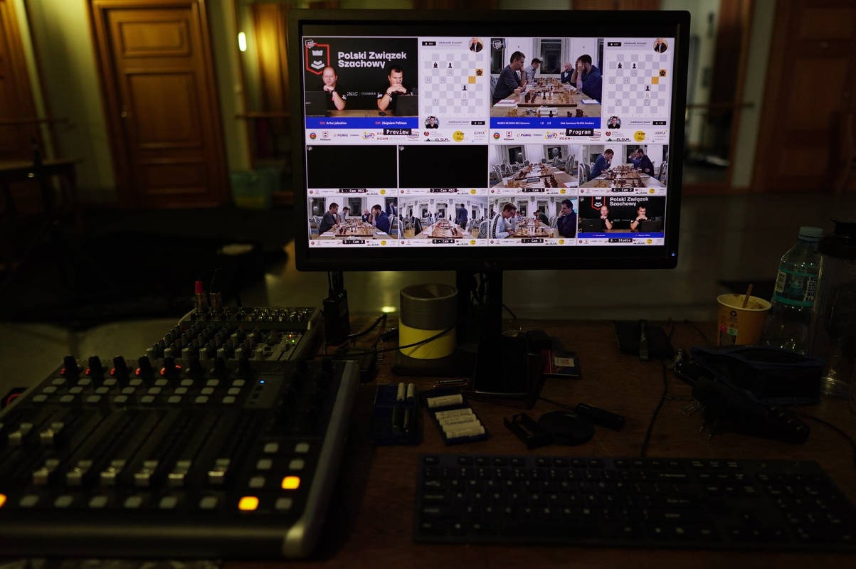 Monitor wyświetlający transmisję szachową z mikserem audio i klawiaturą na stole, widoczne detale konfiguracji studia nagraniowego.