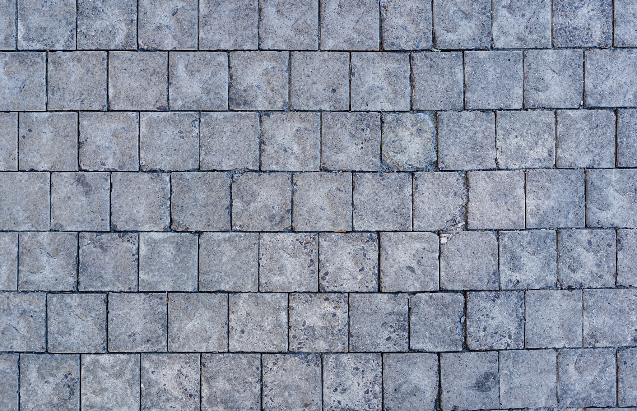 Szara kostka brukowa ułożona w prosty wzór, widoczne szczeliny między kostkami wypełnione drobnym piaskiem.