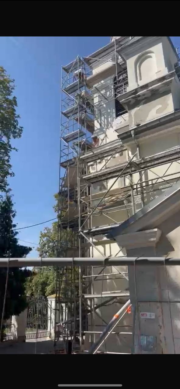 Fragment elewacji zabytkowego budynku sakralnego w trakcie renowacji, z widocznymi rusztowaniami i śladami prac naprawczych na fasadzie.