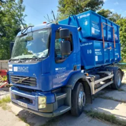 Niebieska ciężarówka z dwoma kontenerami na platformie, z widocznym logo firmy „FRACHT” i numerami kontaktowymi, zaparkowana na betonowym placu w słoneczny dzień.