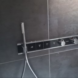 HYDRO-INSTAL-TECH SPÓŁKA Z OGRANICZONĄ ODPOWIEDZIALNOŚCIĄ - Nowoczesna bateria prysznicowa z panelem sterowania na ciemnych, matowych płytkach, widoczna słuchawka prysznicowa z chromowanym wykończeniem i oznaczenia funkcji na panelu.