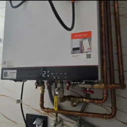 Nowoczesny, biały piec gazowy Viessmann z miedzianymi rurami instalacji, zamontowany na ścianie z marmurowym wzorem. Widoczny wyświetlacz i naklejka 'Connect me!'.