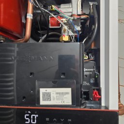 HYDRO-INSTAL-TECH SPÓŁKA Z OGRANICZONĄ ODPOWIEDZIALNOŚCIĄ - Wnętrze nowoczesnego pieca gazowego Viessmann z widocznymi elementami instalacji, przewodami i wyświetlaczem wskazującym temperaturę 50 stopni Celsjusza.