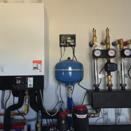 Nowoczesny, biały piec gazowy Viessmann z czarnym panelem sterowania, podłączony do instalacji hydraulicznej z manometrami i pompami obiegowymi. Widoczne elementy instalacji CO.