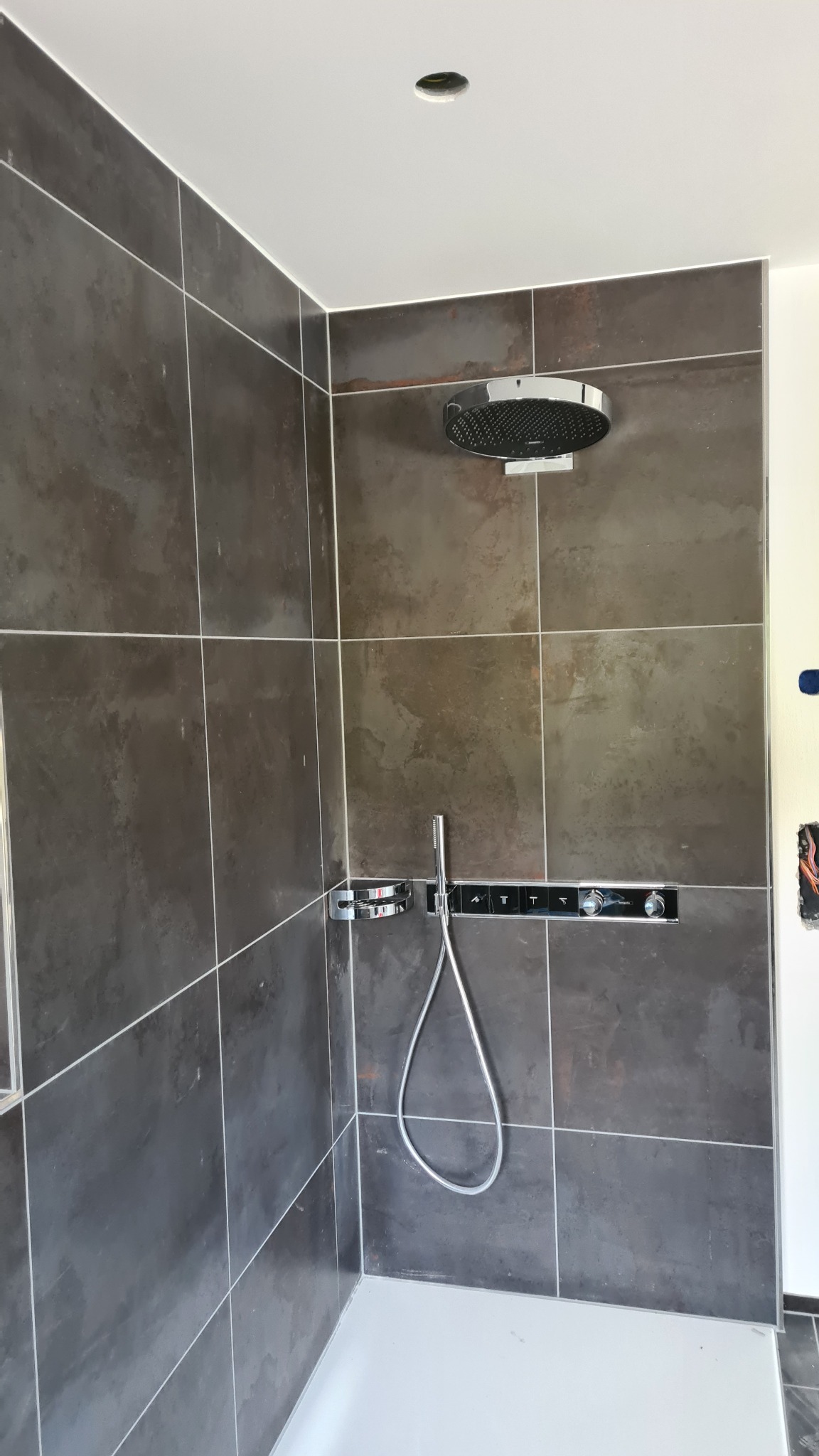 Nowoczesna kabina prysznicowa z deszczownicą i panelami sterującymi wkomponowanymi w ciemne, matowe płytki, z widocznym fragmentem instalacji elektrycznej po prawej stronie.