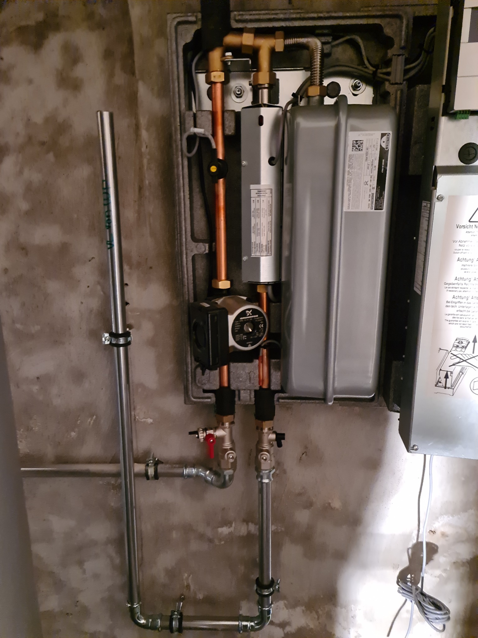 Zamontowany piec gazowy kondensacyjny z widocznymi rurami miedzianymi i elementami instalacji, zamocowany na szarej ścianie z widocznymi zaciekami i niedoskonałościami.