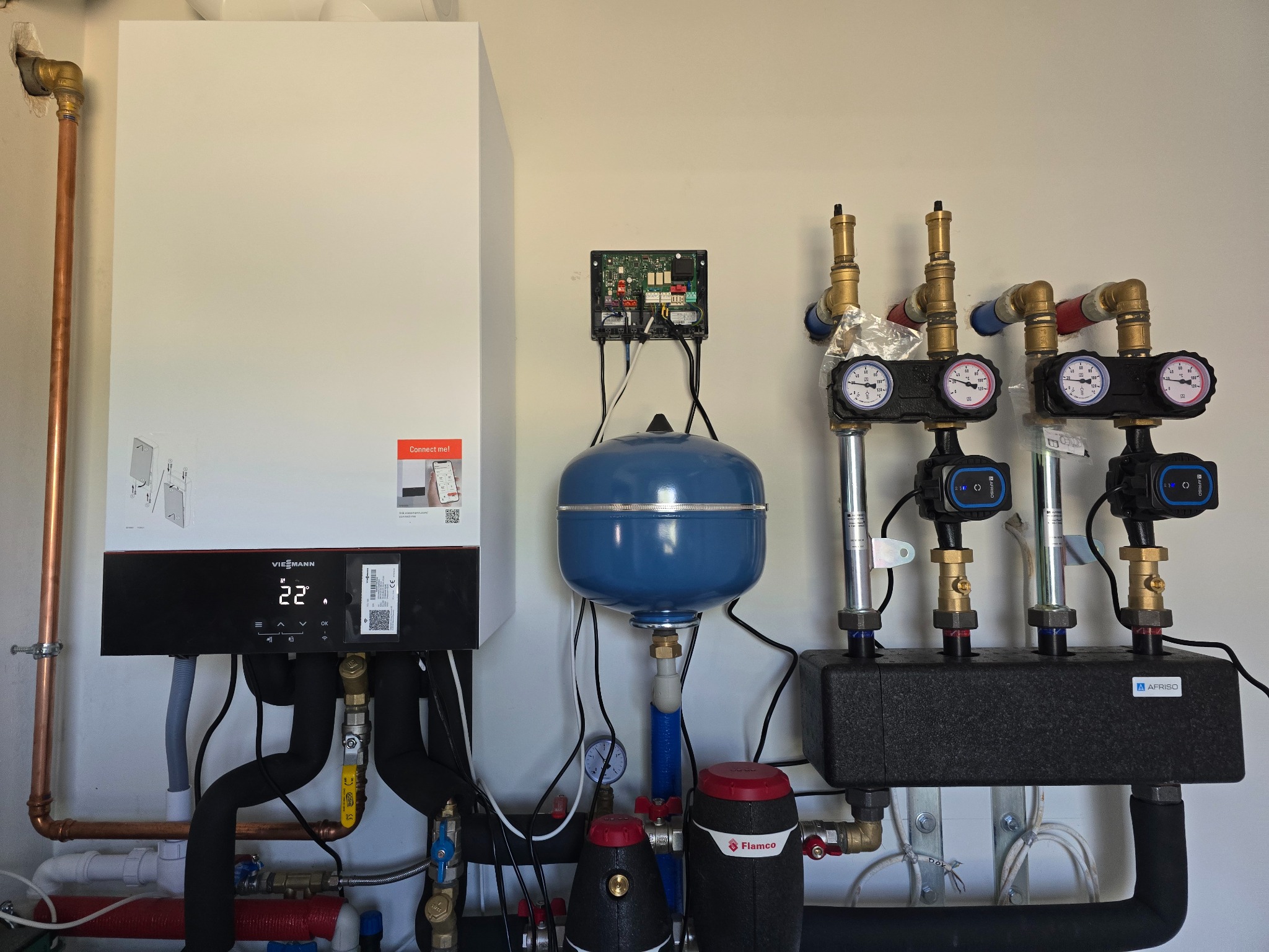 Nowoczesny, biały piec gazowy Viessmann z czarnym panelem sterowania, podłączony do instalacji hydraulicznej z manometrami i pompami obiegowymi. Widoczne elementy instalacji CO.