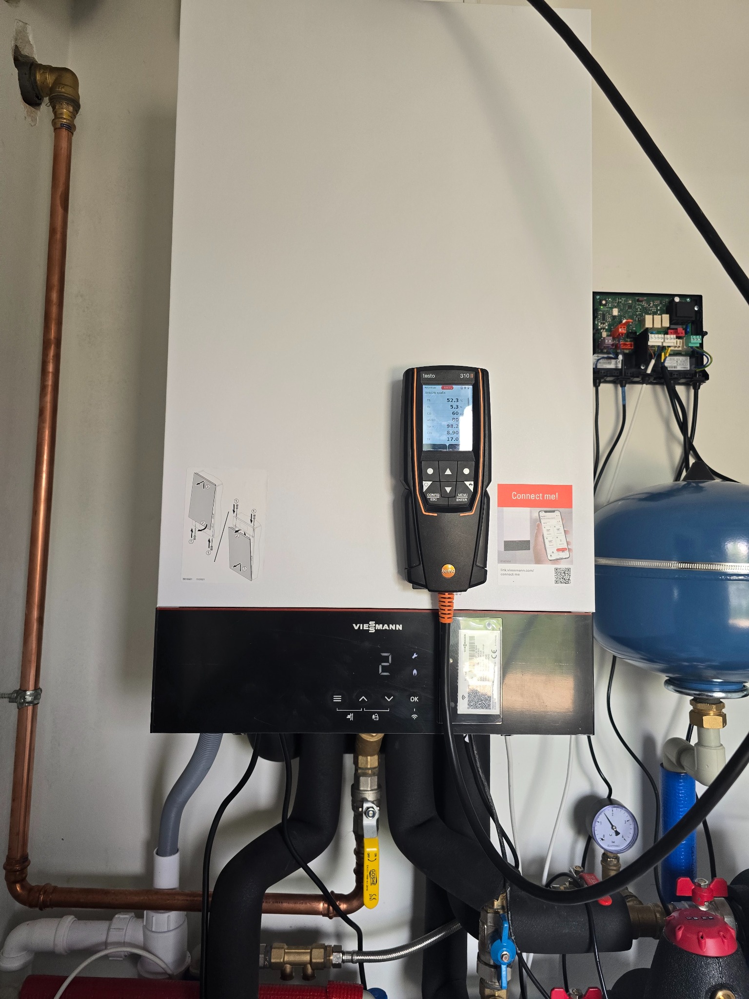 Biały piec gazowy Viessmann z podłączonym analizatorem spalin Testo 310 II, widoczne rury miedziane i elementy instalacji. Pomiar parametrów pracy kotła.