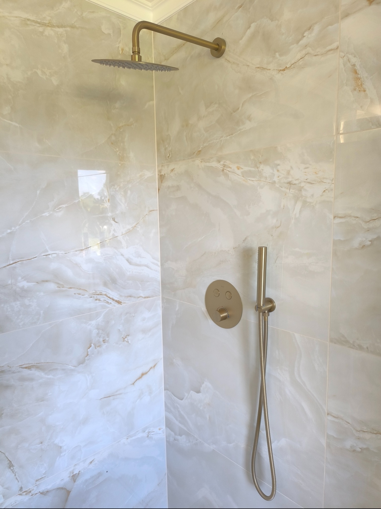 Wykończona kabina prysznicowa z marmurowymi płytkami, deszczownicą i zestawem prysznicowym w kolorze szczotkowanego złota.