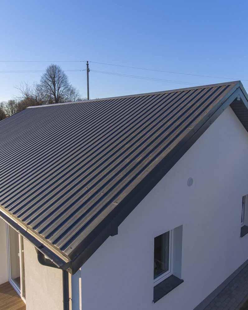 Dom jednorodzinny z nowym, ciemnoszarym dachem z blachy trapezowej, widok z góry, błękitne niebo w tle.