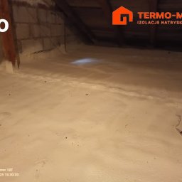 Termo-metr Tomasz Kudła - Poddasze po natrysku pianki izolacyjnej, widoczne krokwie i fragment ściany z cegieł, w rogu logo firmy wykonującej izolację.