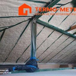Termo-metr Tomasz Kudła - Poddasze po ociepleniu pianką PUR, widoczne krokwie i izolacja natryskowa. Na pierwszym planie zabezpieczone kable. Widok z dołu na ocieploną konstrukcję dachu.