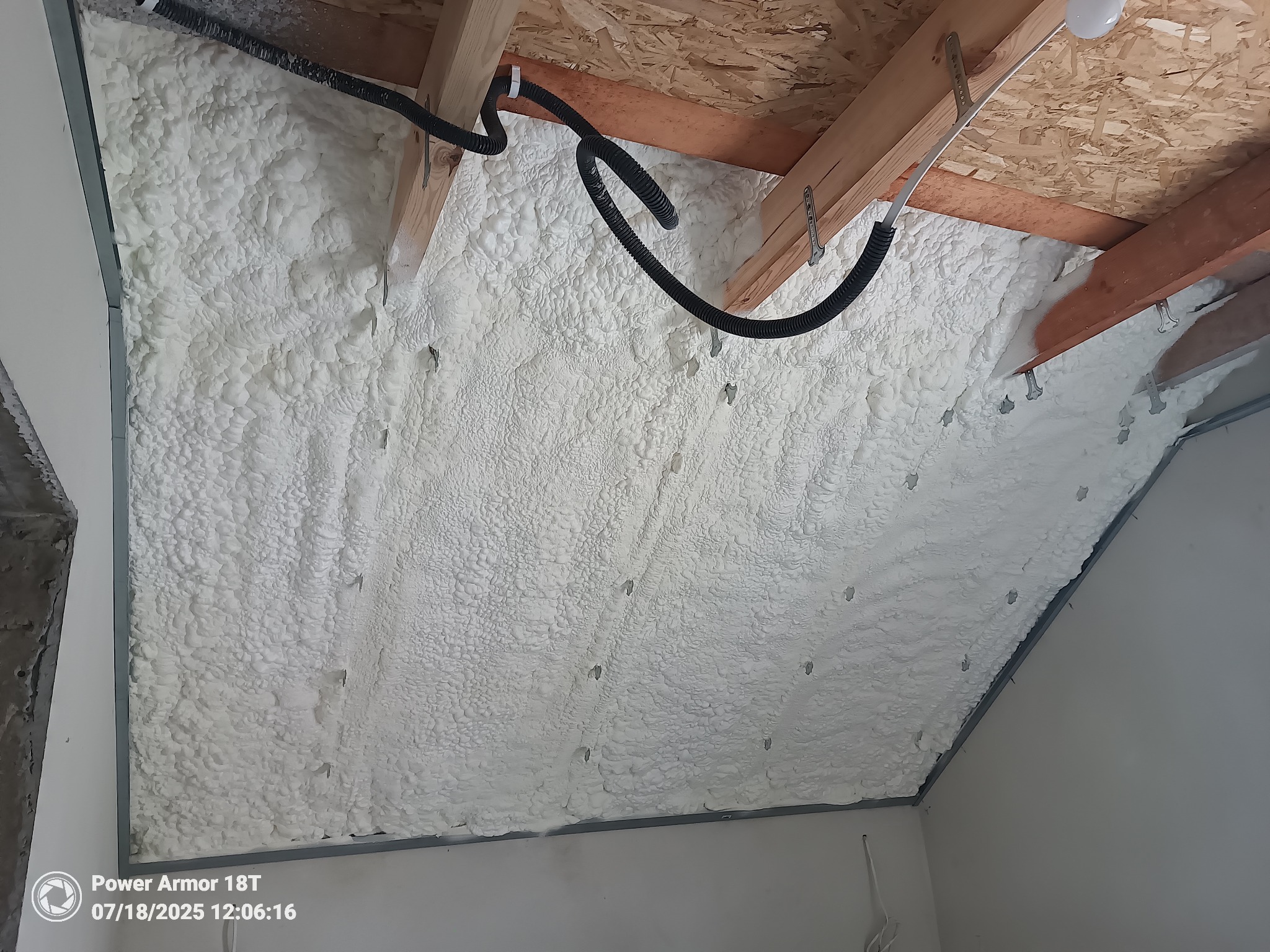 Poddasze ocieplone białą pianką PUR, widoczne elementy konstrukcyjne dachu i instalacja elektryczna w peszlu. Metalowe profile mocujące.